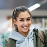 young happy woman at refrigerated section of supermarket looking at camera e1681373784115